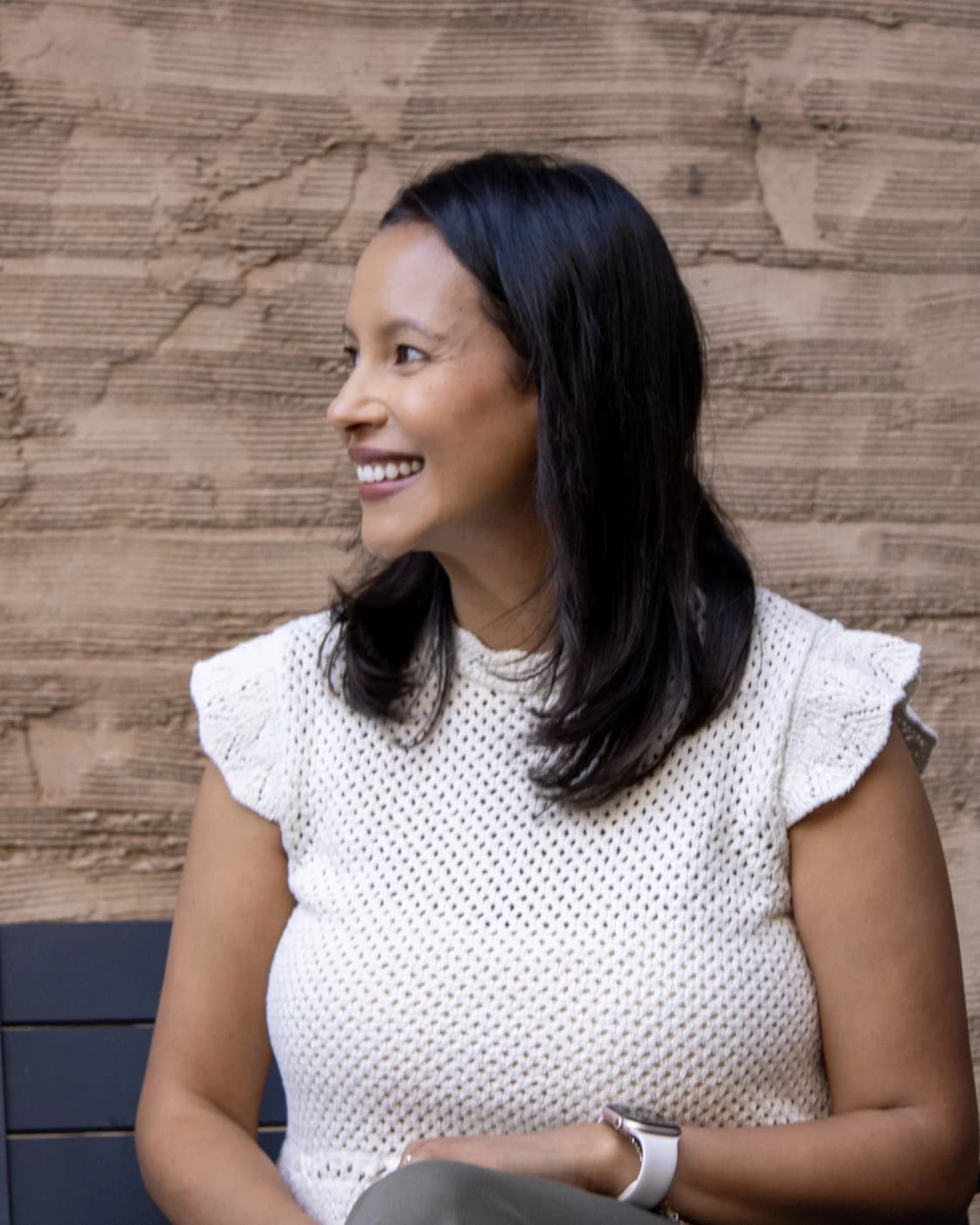 Selma Beirne smiling and looking off to the side, seated against a warm, textured wall.